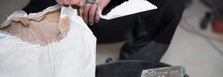 Person nimmt mit Kelle Pulver aus Sack und füllt es in einen Eimer